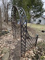 Front three-quarter view of the metal lattice archway installed outdoors on leaf-covered ground