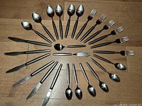 Full set of Eldan flatware including spoons, forks, knives with black handles and serving pieces arranged on wood floor