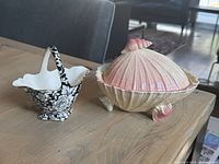 Both ceramic pieces shown on wooden table with background of chairs and floor.