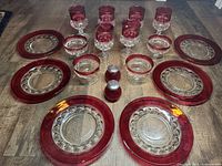 Top-down view of six ruby glass salad or dessert plates arranged in a circle with six ruby glass wine glasses in the center and some sorbet glasses and salt and pepper shakers also included