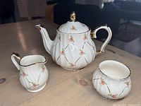 Teapot with creamer and sugar bowl arranged on table showing floral design and gold trim