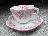 Cup and saucer set showing floral pink pattern on white porcelain, side view.