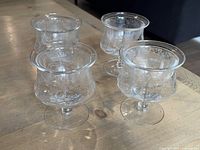 Four clear etched shrimp cocktail glasses on table, showing floral/vine pattern etching, short stems, and flared rims.