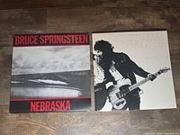 Image shows two Bruce Springsteen vinyl albums: 'Nebraska' with a black and white cover with red text on left, and 'Born To Run' with a white cover and photo of Springsteen on right.