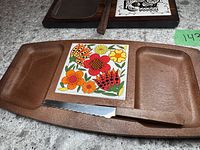 Close view of brown stone cheese tray with colorful floral tile insert and serrated knife with matching handle.