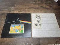 Photo showing both Pink Floyd albums side by side: 'The Dark Side of the Moon' on left with black prism cover, and 'The Wall' on right with white brick pattern cover and handwritten style label.