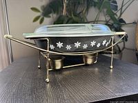 Side view of black Pyrex dish on heating stand showing white snowflake pattern and metal candle holders below.