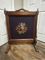 Front view of antique wooden fire screen with central framed tapestry panel showing floral design.