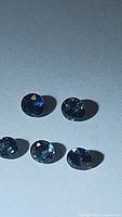Five round cut blue sapphires with vibrant deep blue color placed on a light surface, showing clarity and facets.