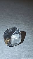 Clear cushion-shaped quartz with concave facets, showing light reflections and high clarity on textured background.