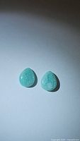 Two pear-shaped Amazonite cabochons in soft blue-green tones shown on white background under direct light, revealing surface and internal texture details.