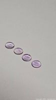 Four oval cabochon purple amethyst gemstones arranged in a row on a light background showing color and cut