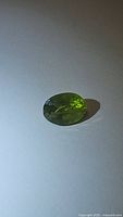 Oval faceted apple green Peridot gemstone shown on white background, highlighting its rich green color and inclusions.