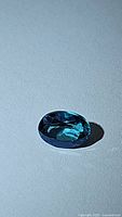 Close-up photo of an oval faceted blue topaz gemstone showing its deep lagoon aqua blue color and clarity