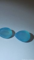 Close up photo of two natural Arctic Blue Chalcedony pear cut gemstones showing their color and shape.