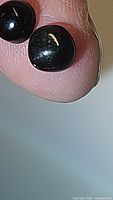Close-up photo showing two round cabochon black star diopside gemstones with visible star effect on finger tip.