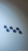 Top down view of six natural blue sapphire round cabochons on a white background showing size and color.