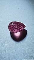 Close-up photo of the briolette cut pink red ruby showing facets and shape from an angle.