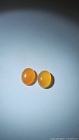 Two natural oval cabochon carnelian gemstones showing mandarin orange color and smooth cabochon cut, well-matched pair.