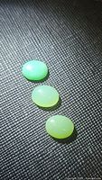Three natural oval chrysoprase cabochons on textured black background, showing their translucency and light green shades.