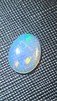 Oval natural Ethiopian crystal opal, showing multicolored flash under light on a textured black background.