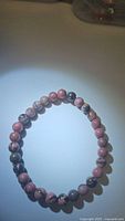Natural rhodochrosite bead bracelet arranged in circle on a plain light background showing pink and gray patterned round beads.