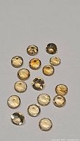 Top down photo of 16 natural golden citrine round faceted gemstones, varying shades from pale yellow to deeper amber, size approximately 2mm to 3mm.