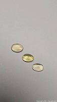 Three natural lemon citrine oval cabochon gemstones on white background showing light yellow color and polished smooth cabochon cuts.