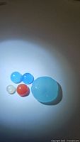 Photo showing five polished natural mixed gemstones illuminated on a white surface including a large light blue chalcedony, two small blue stones, one small white moonstone, and one small orange carnelian.