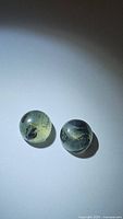 Pair of natural round moss agate cabochon gemstones placed on a plain white background, showing translucent quality with black dendritic moss inclusions inside each.
