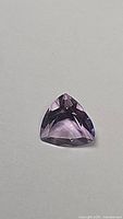 Close-up photo of single natural purple amethyst gemstone with trillion cut on neutral background.