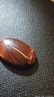 Close-up photo of a natural red tiger's eye oval cabochon gemstone showing its polished smooth surface with chatoyant bands under light on a black background.