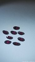 Photo showing eight oval cut rhodolite garnet gemstones arranged on a flat surface under a focused light source.