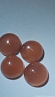 Four round polished strawberry quartz cabochons on a flat surface showing glossy smooth finish and reddish-pink color.
