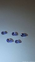 Five pear-shaped natural tanzanite gemstones arranged on a white surface showing their pear-cut, purple-blue color, and clarity.
