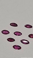 Nine natural untreated marquis cut rubies laid out on a flat surface, showing their marquis shape, faceted cuts, and pink-red color.