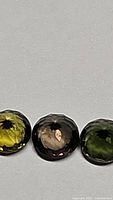 Three faceted round cut natural untreated tourmalines in different green shades on a plain background.