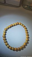 Top-down photo showing circular arrangement of yellow wood grain Jasper beads on stretch cord on white surface.
