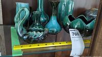 Collection of Blue Mountain Pottery vases and basket piece displayed on a glass shelf with measuring tape showing size scale.