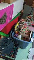 Grey bin containing assorted boxed ornaments, light spool, linens and centerpiece