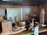 Wooden animal and bird figures including whale, toucan, bowls, and stands arranged on a wooden shelf.