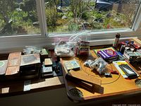 Photo showing all game items spread out on a wood surface by a window, including boards, boxes, playing cards in plastic bags, and a cribbage board.