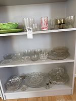 Shelves with assorted glassware and green ceramic serveware: bowls, platters, drinking glasses, salt and pepper shakers
