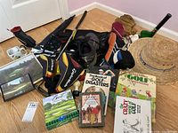 Overview of golf related books, club covers, shoes, hat, golf balls, and framed photos on floor