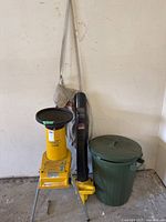 Full view of the yellow AL-KO mulcher shredder, black leaf blower tube attached, and green garbage can side by side against a wall.