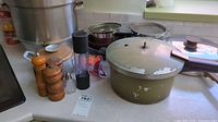Photo showing large aluminum pressure cooker, green saucepan with lid, wooden salt & pepper grinders, clear glass salt shaker, and fire alert spray.