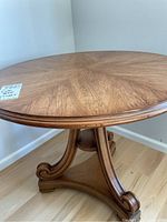 Photo of full wood side table showing round top and scroll pedestal legs on wood floor