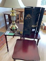 Photo showing a brass and white ceramic table lamp, the smallest nesting table, and the black oriental style folding table divider with gold floral accents.