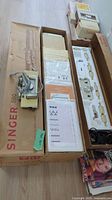 Top view of Singer 560 knitting machine and original box with multiple attachments, books and pattern cards laid out inside box.