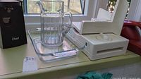 Photo showing electric food slicer, glass jug, and clear rectangular glass casserole dish on a window sill.